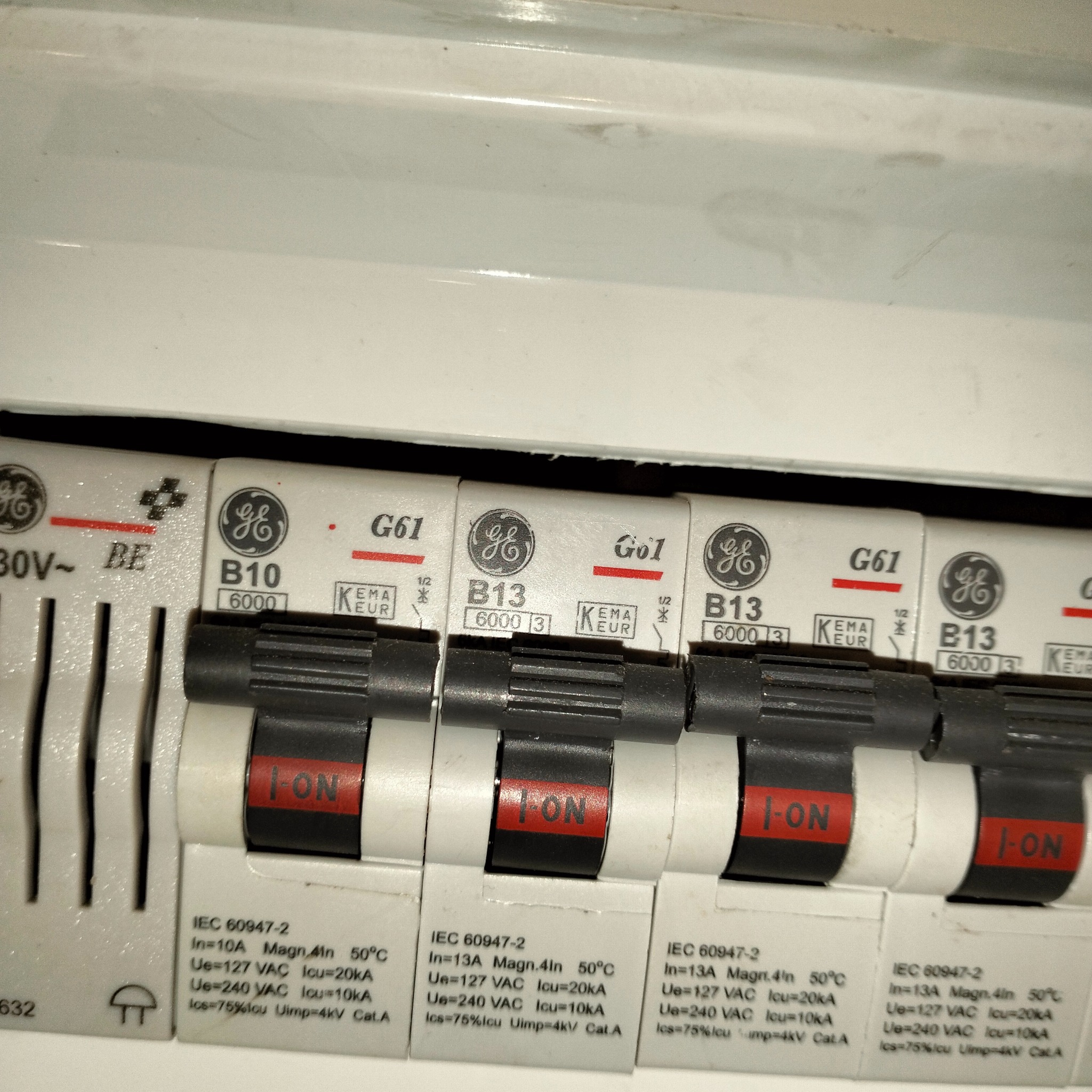 Szczegółowe ujęcie czterech wyłączników nadprądowych firmy GE z oznaczeniami B10 i B13, w pozycji ON, zamontowanych w rozdzielnicy elektrycznej, widoczne parametry techniczne na obudowie.