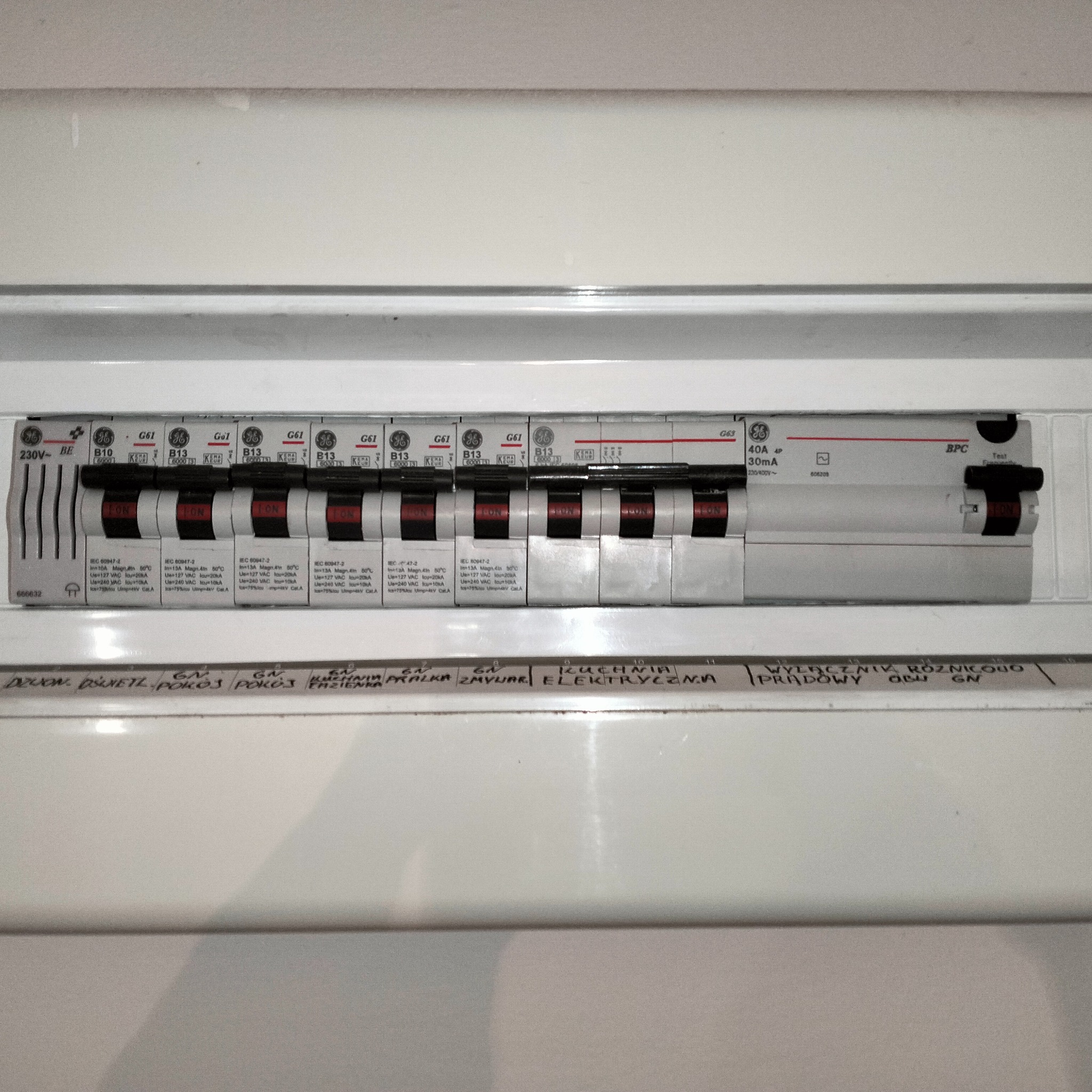 Tablica rozdzielcza z bezpiecznikami i wyłącznikiem różnicowoprądowym, widoczne oznaczenia obwodów wykonane odręcznie.