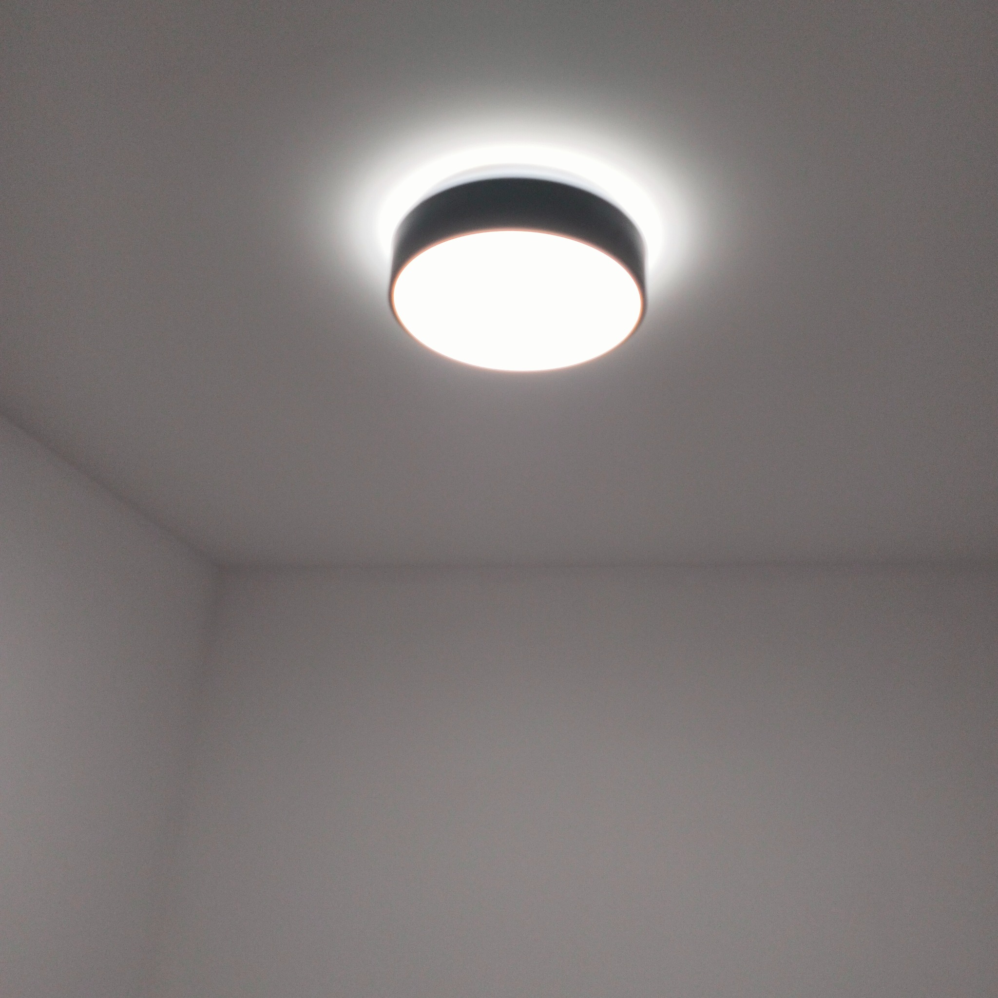 Okrągła lampa sufitowa z czarną obudową, świecąca białym światłem, zamontowana na białym suficie w pomieszczeniu w Braniewie.