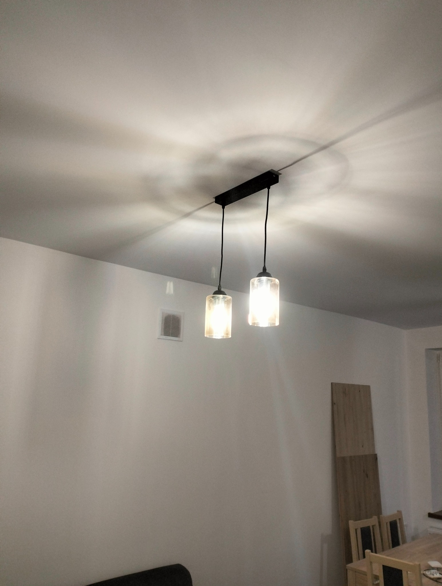 Dwa szklane klosze lamp wiszących na czarnej listwie oświetleniowej, zamontowane na białym suficie, rzucające okrągłe cienie światła.