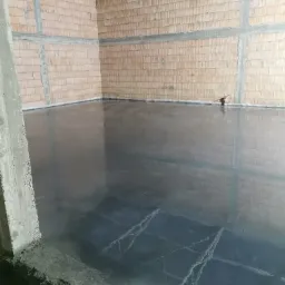 Świeżo wylana, gładka posadzka przemysłowa w surowym pomieszczeniu z ceglanymi ścianami i widocznymi betonowymi wzmocnieniami, z refleksami światła na powierzchni betonu.