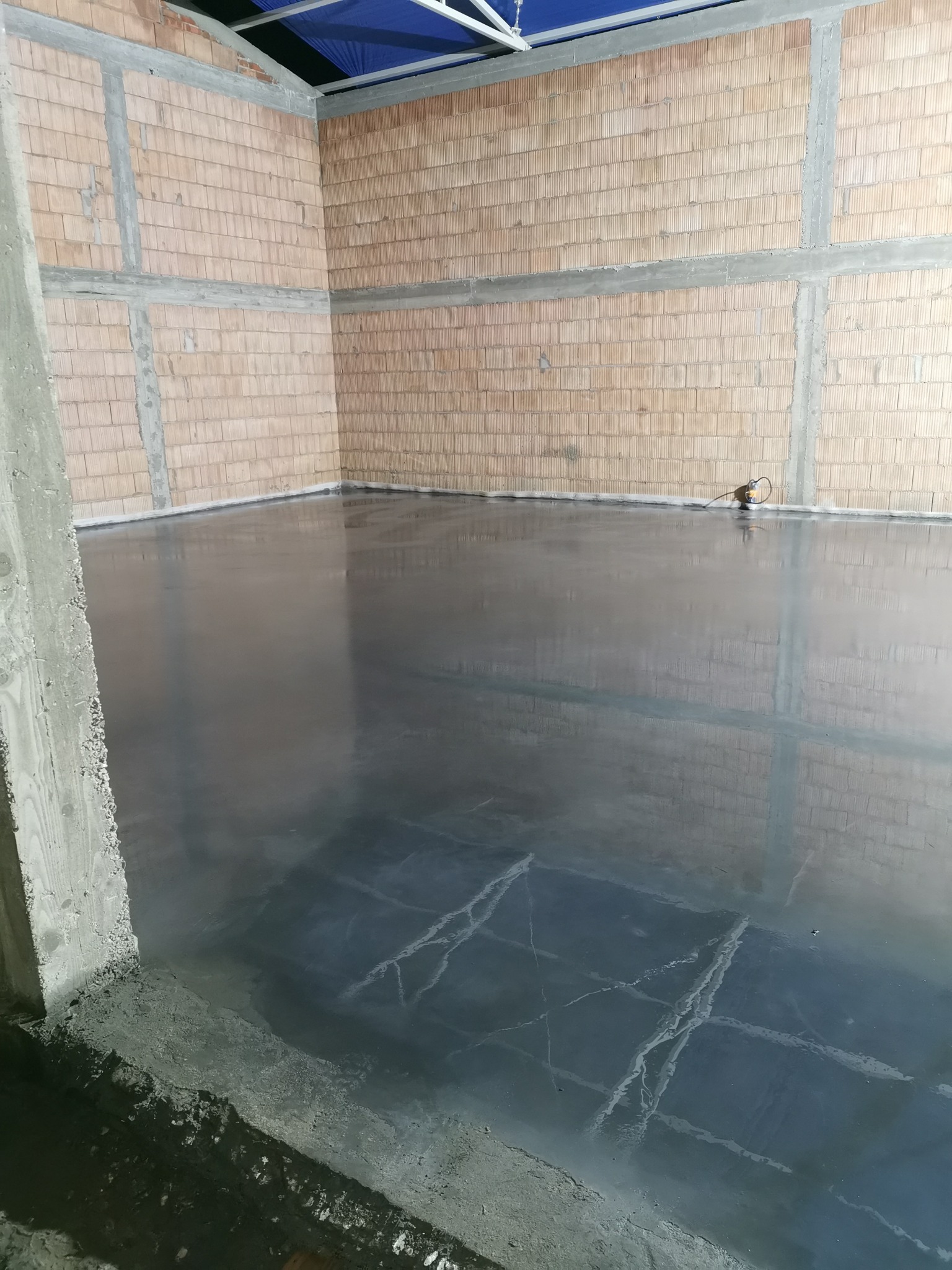 Świeżo wylana, gładka posadzka przemysłowa w surowym pomieszczeniu z ceglanymi ścianami i widocznymi betonowymi wzmocnieniami, z refleksami światła na powierzchni betonu.