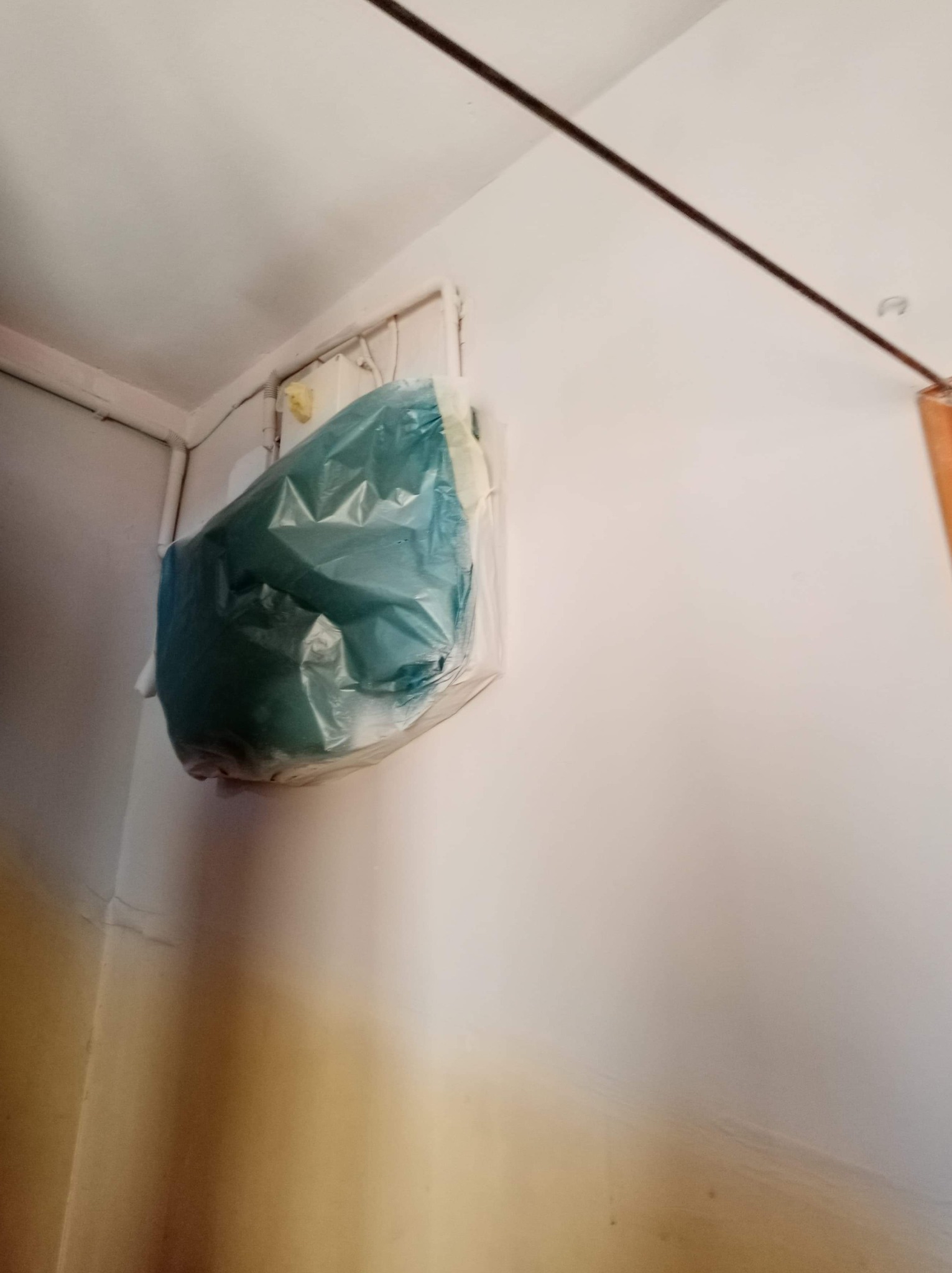 Grzejnik zabezpieczony folią malarską podczas prac remontowych w pomieszczeniu z białymi ścianami i sufitem.