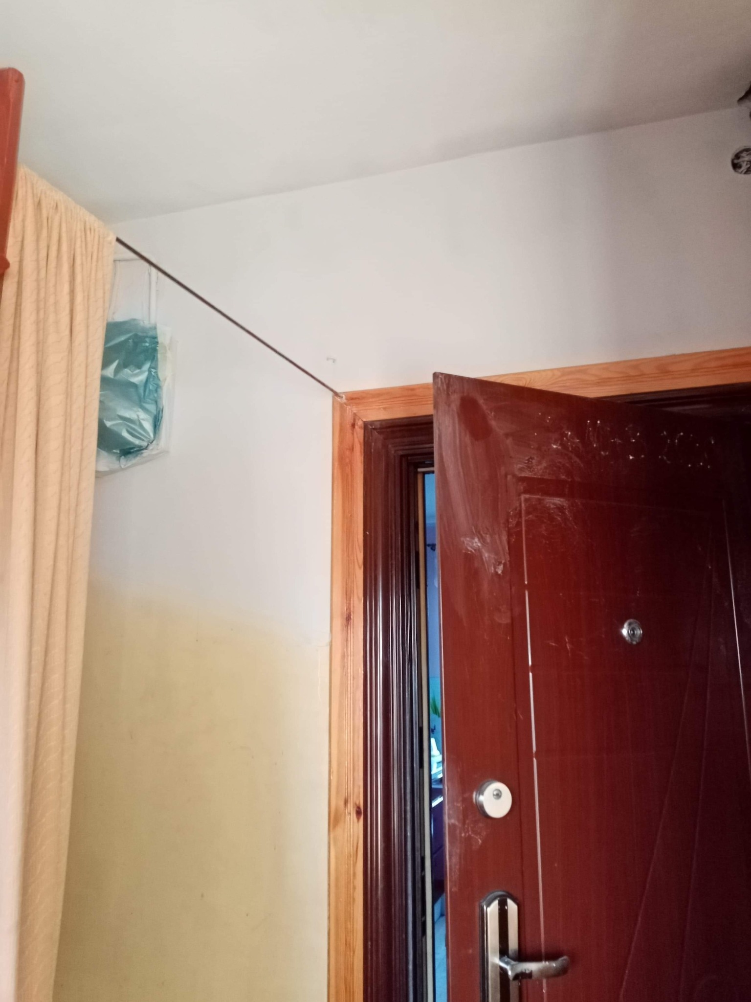 Otwarta, brązowa, częściowo zabrudzona farbą po remoncie, wewnętrzna strona drzwi wejściowych z metalową klamką i wizjerem, widok na wnętrze mieszkania, obok fragment ściany z zasłoniętym folią...