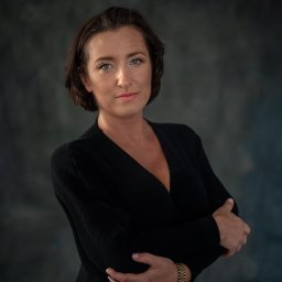 Studio Urody Endorfina - Portret kobiety o niebieskich oczach, w czarnej sukience z rękawami skrzyżowanymi na piersiach, z zegarkiem na ręku, na tle ciemnego, niebieskiego tła.