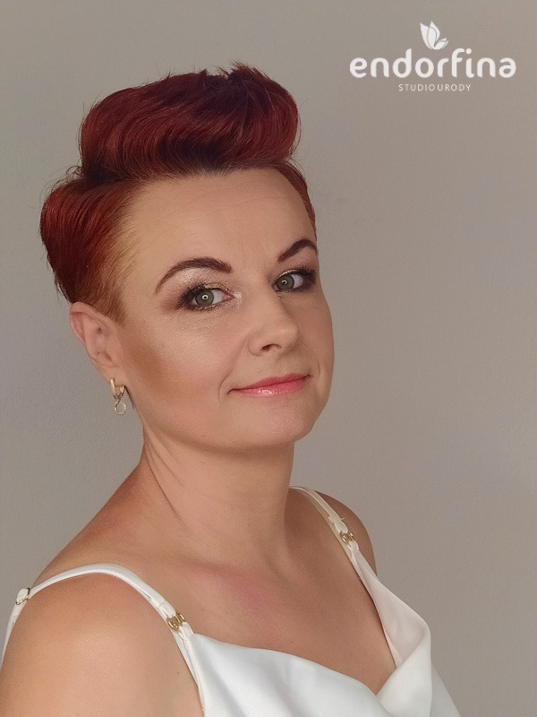 Portret kobiety z krótkimi, rudymi włosami i delikatnym makijażem, prezentującej efekt stylizacji w studiu urody.