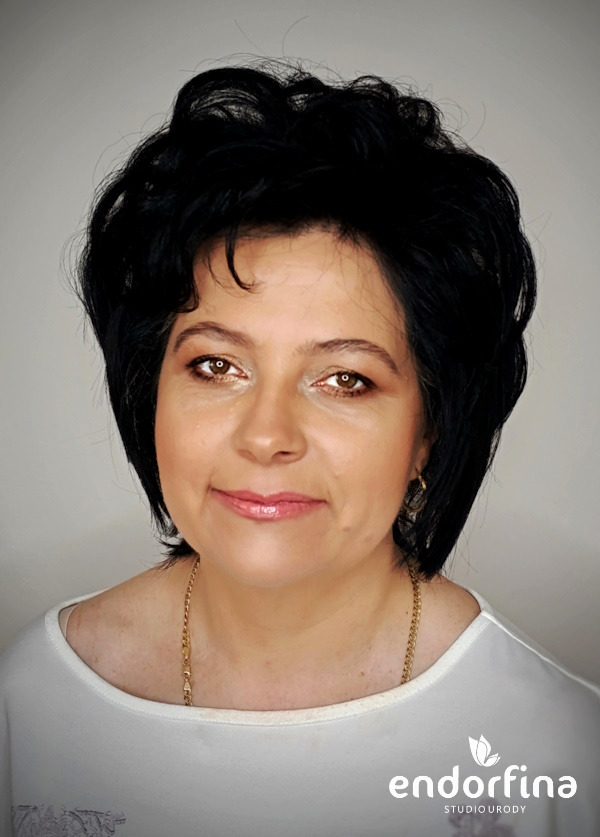 Portret kobiety z delikatnym makijażem, brązowe oczy, czarne włosy, złoty łańcuszek. Logo studia urody w prawym dolnym rogu.