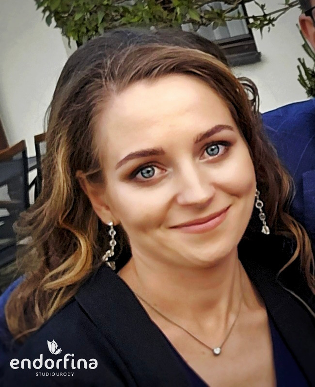 Portret uśmiechniętej kobiety z delikatnym makijażem oczu, srebrną biżuterią i logo studia urody w lewym dolnym rogu. Naturalne światło.