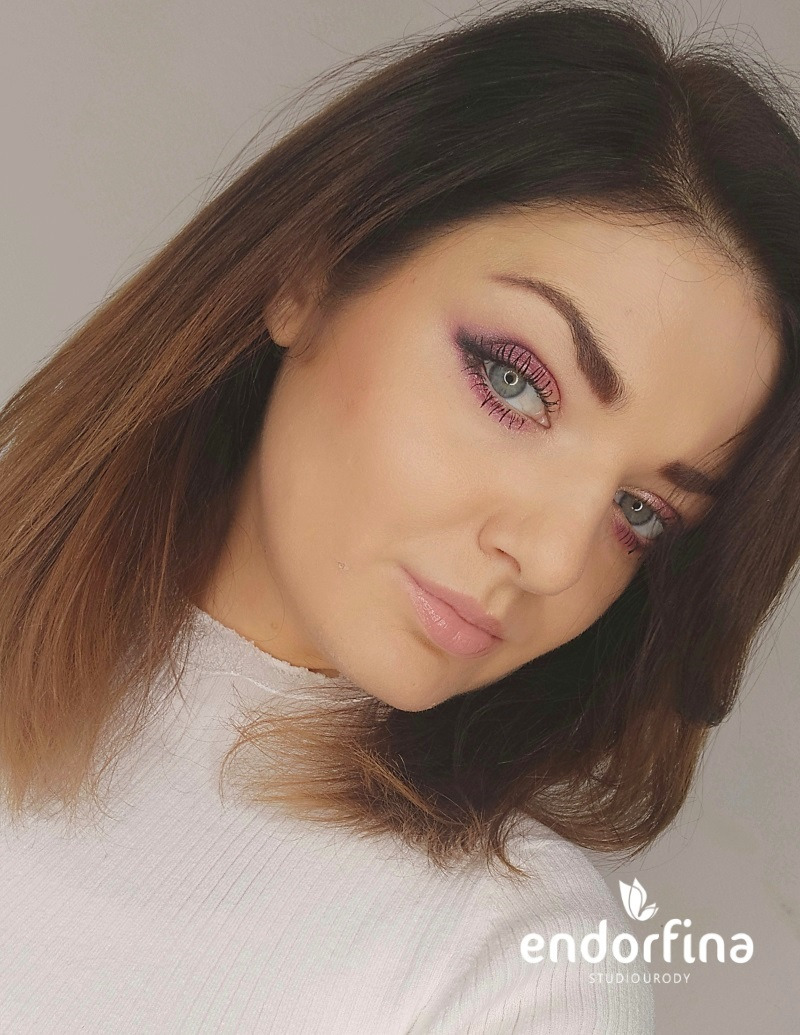 Portret kobiety z profesjonalnym makijażem oczu w odcieniach różu i fioletu. Widoczny logo salonu kosmetycznego w prawym dolnym rogu.