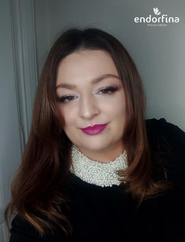 Portret kobiety z profesjonalnym makijażem, w tym z wyrazistą różową szminką i subtelnym makijażem oczu, prezentujący efekt finalny usługi. Logo salonu w prawym górnym rogu.