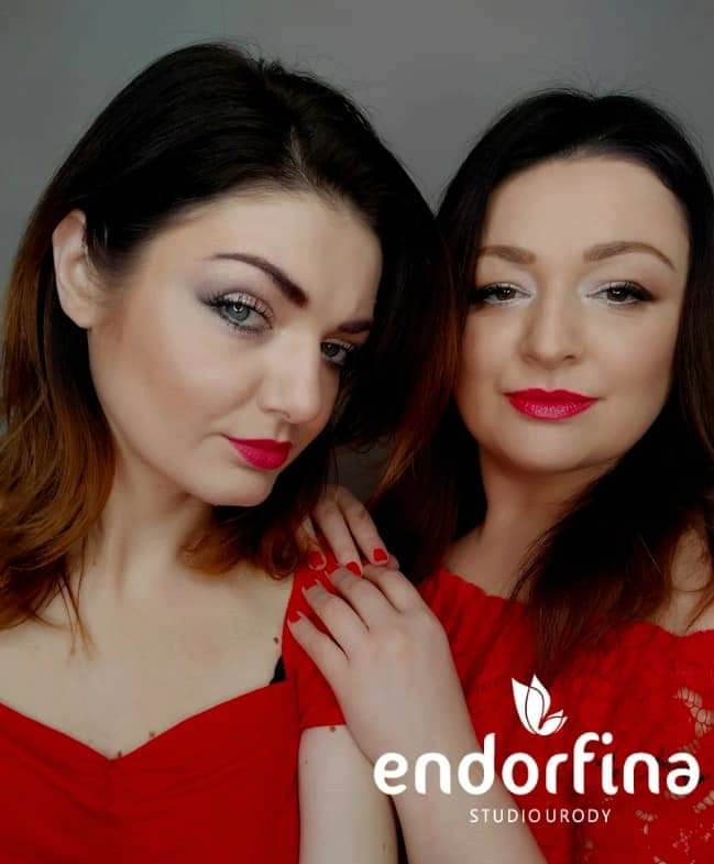 Dwie kobiety z czerwonymi ustami i profesjonalnym makijażem oczu, pozujące w czerwonych bluzkach. Widoczne logo studia urody.