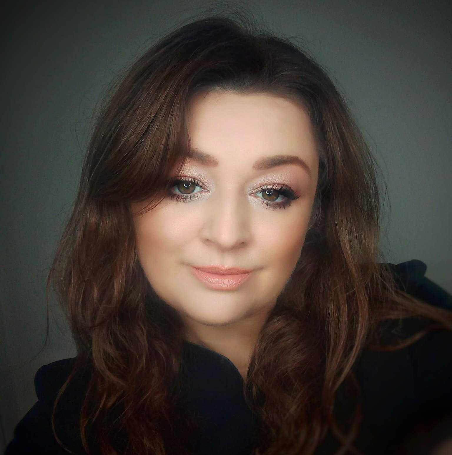 Portret kobiety z delikatnym makijażem, brązowe włosy opadają na ramiona. Uwagę przyciągają starannie podkreślone oczy i subtelny odcień ust.