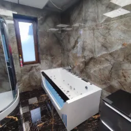 Luksusowa łazienka z kabiną prysznicową i wanną z hydromasażem, wykończona marmurowymi płytkami w odcieniach brązu i czerni, z ciemną, błyszczącą podłogą.