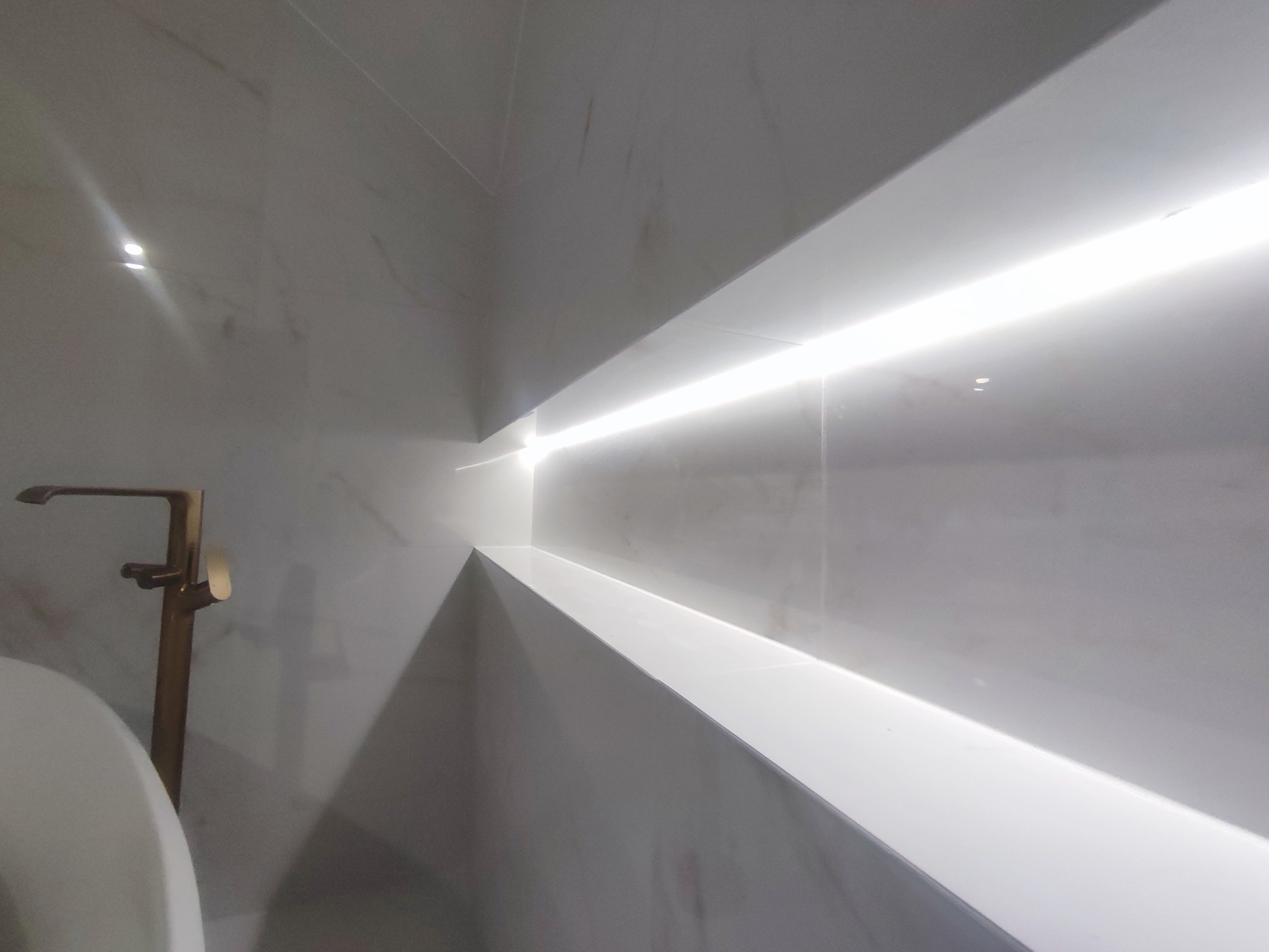 Nowoczesna łazienka: białe marmurowe płytki, złota bateria i podświetlana półka wnękowa. Minimalistyczny design i eleganckie wykończenie.