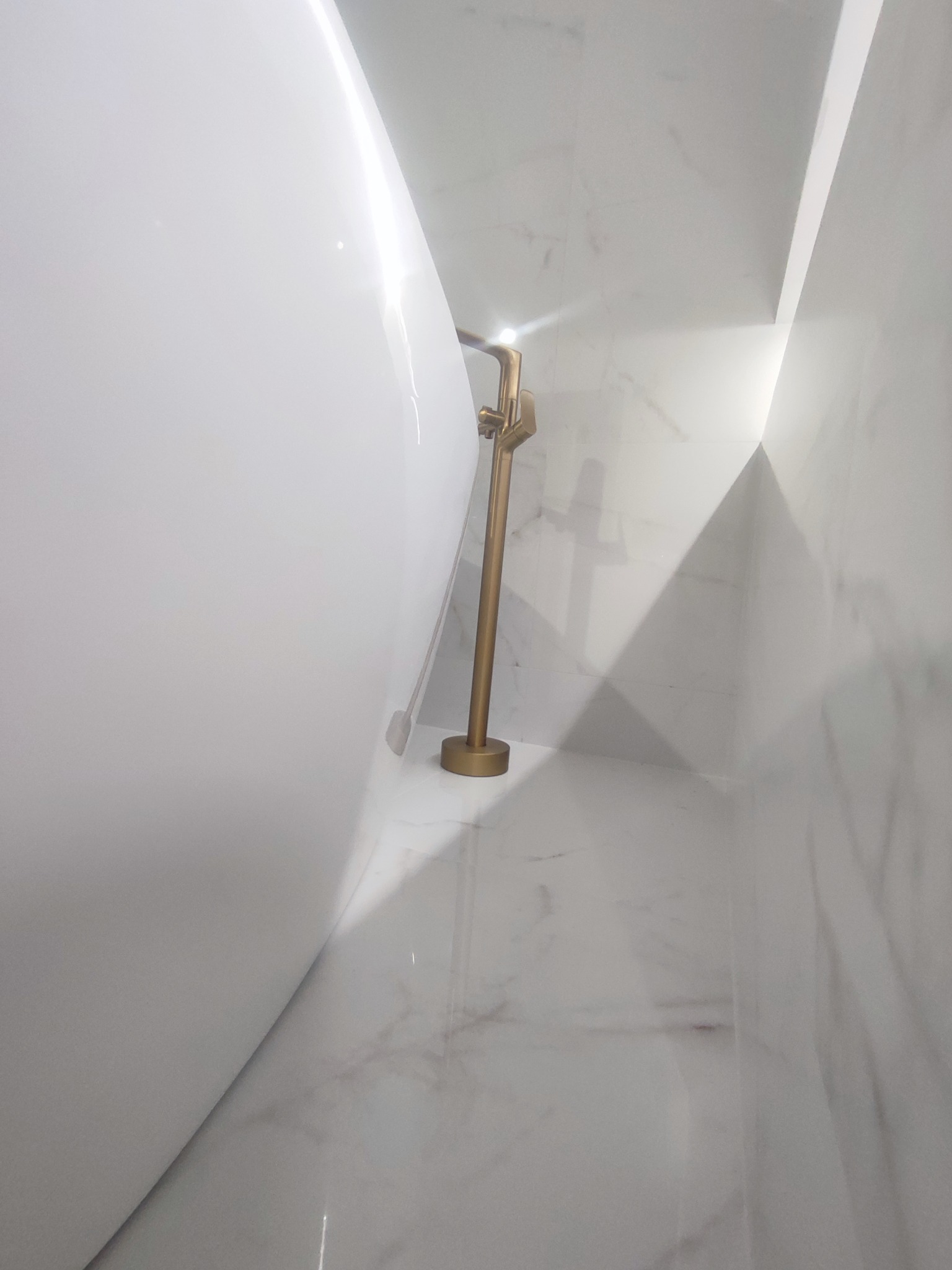 Biała wanna wolnostojąca z złotą armaturą w nowoczesnej łazience wykończonej marmurem.