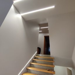 DOM BUD - Schody z podświetleniem LED w Tłuszczu. Nowoczesne wykończenie wnętrza, minimalistyczny design z liniami świetlnymi na suficie i wzdłuż schodów.