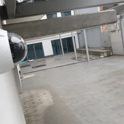 Kamera monitoringu kopułkowa, zamontowana na ścianie zewnętrznej budynku w deszczowy dzień, widoczne krople wody na obudowie i otoczeniu.