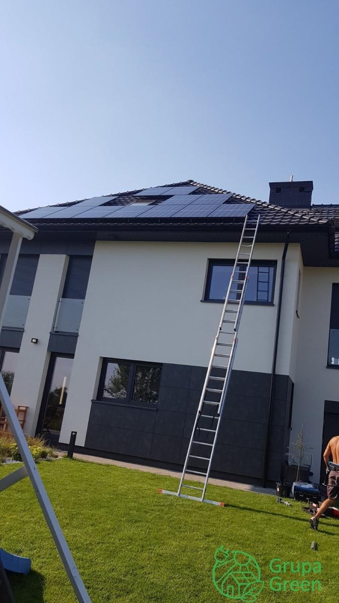 Montaż paneli słonecznych na dachu dwukondygnacyjnego domu, widoczna drabina oparta o ścianę, fragment trawnika i sprzęt montażowy.