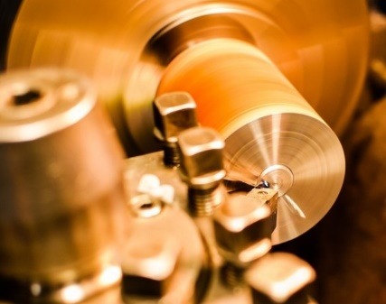 Toczenie metalu na tokarce; wióry odchodzą od obracającego się elementu, narzędzie tokarskie w zbliżeniu, oświetlenie warsztatowe.