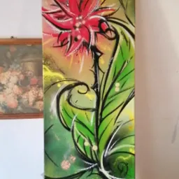 Wertykalny obraz przedstawiający stylizowany czerwony kwiat z zielonymi liśćmi na rozmytym, zielono-żółtym tle z czarnymi konturami, umieszczony obok obrazu w ramie wiszącego na ścianie.