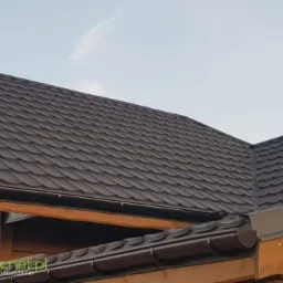 Brązowy dach z blachodachówki modułowej, widoczne rynny i komin wentylacyjny, drewniana konstrukcja dachu.