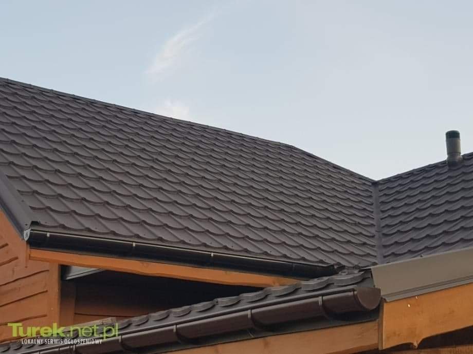 Brązowy dach z blachodachówki modułowej, widoczne rynny i komin wentylacyjny, drewniana konstrukcja dachu.