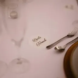 Elegancko nakryty stół z imienną wizytówką 'Beata Nowak', srebrnymi sztućcami z tłoczeniami i szklanym świecznikiem w tle.