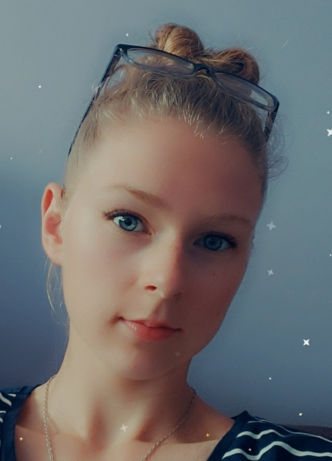 Portret młodej kobiety z blond włosami spiętymi w kok, z okularami na głowie, patrzącej w obiektyw, na tle jednolitego, lekko niebieskiego tła, z dodanymi cyfrowo efektami świetlnymi w kształcie...