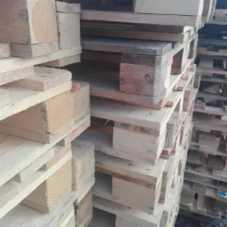 Stos drewnianych palet o różnym odcieniu drewna, ułożonych jeden na drugim, widok z bliska.