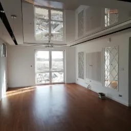 Nowoczesne wnętrze z drewnianą podłogą, lustrzanymi dekoracjami ściennymi i widokiem z okna na plac budowy.