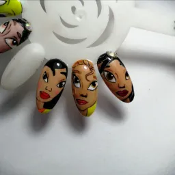 Prezentacja zdobionych tipsów z motywami twarzy postaci z bajek na białym tle, umieszczonych na plastikowym wzorniku.