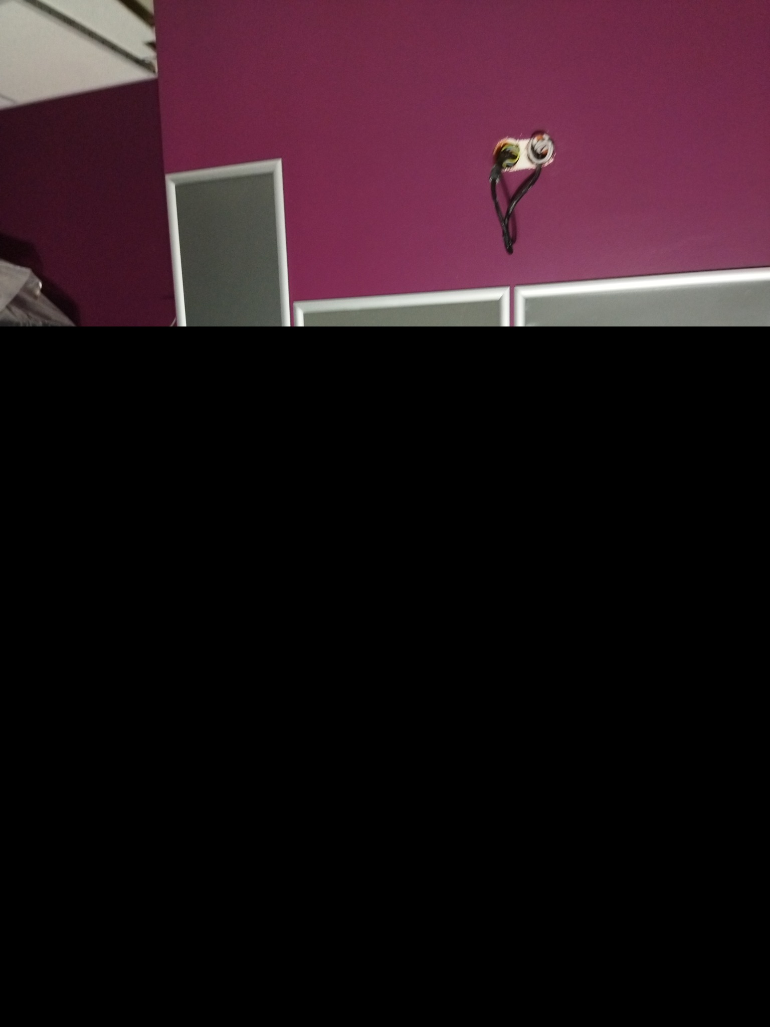 Fioletowa ściana z niedokończonymi gniazdkami elektrycznymi i fragmentem szarej zabudowy.