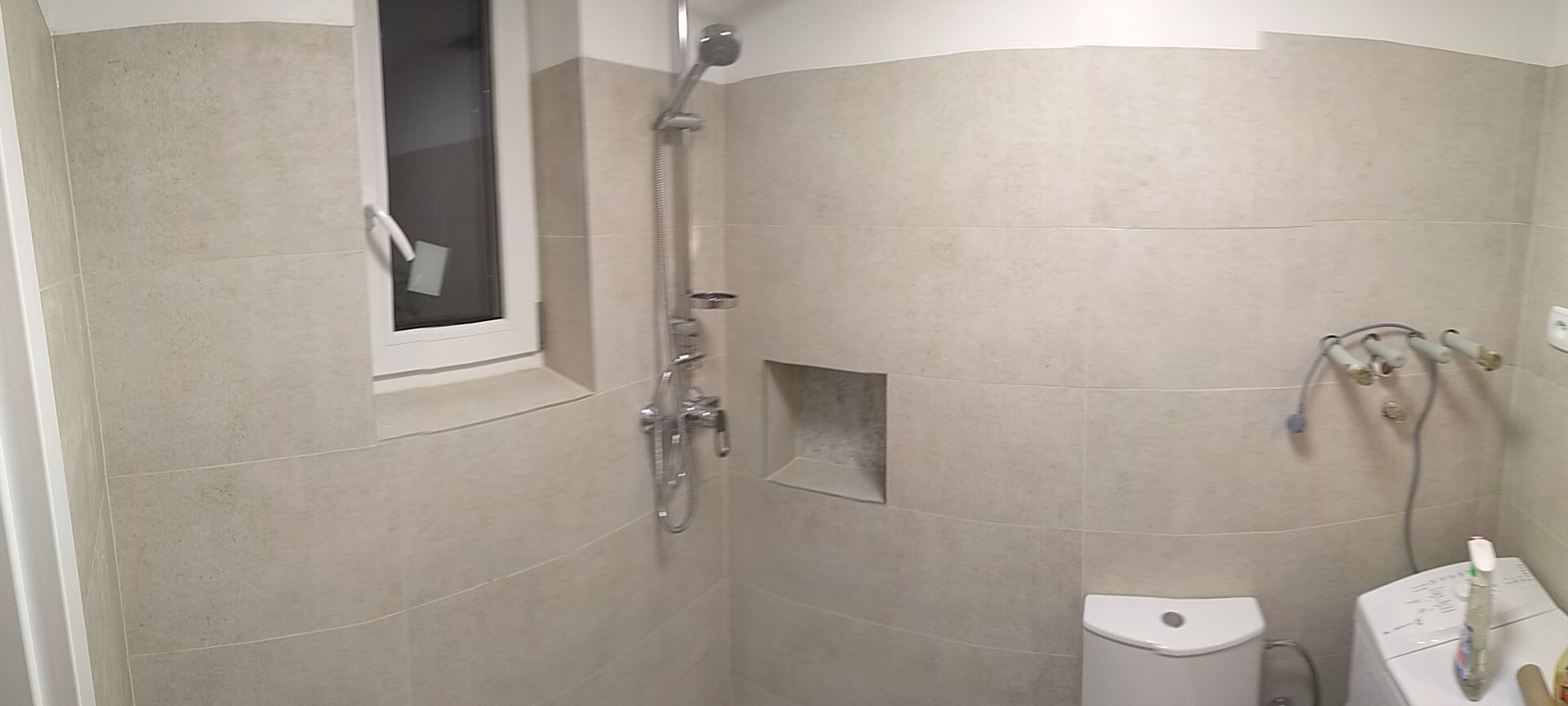 Jasna łazienka po remoncie z beżowymi płytkami, wnęką w ścianie, kabiną prysznicową i pralką w rogu.