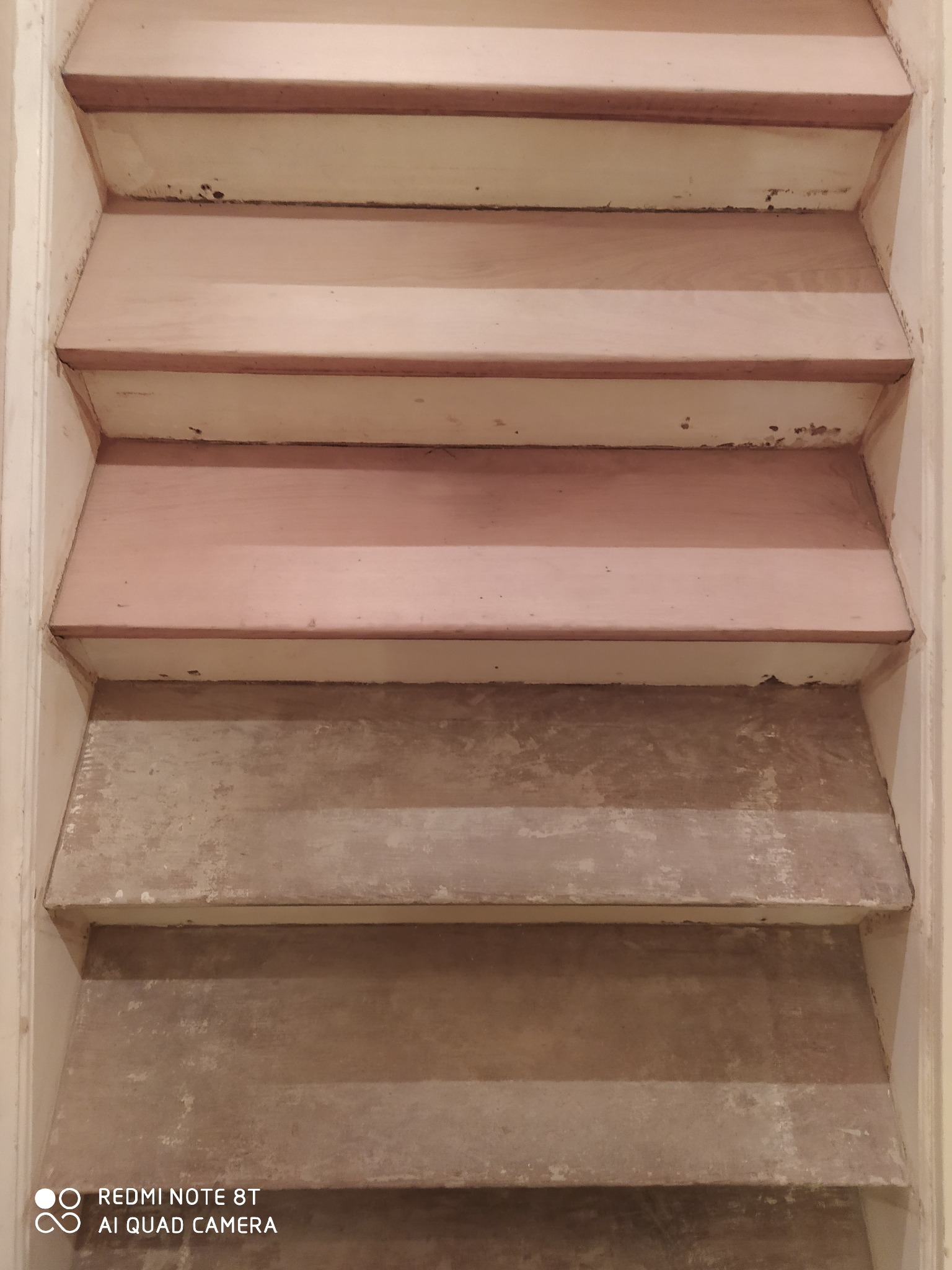 Schody w trakcie renowacji, widoczne ślady starej farby i przygotowanie do malowania, ujęcie od dołu.