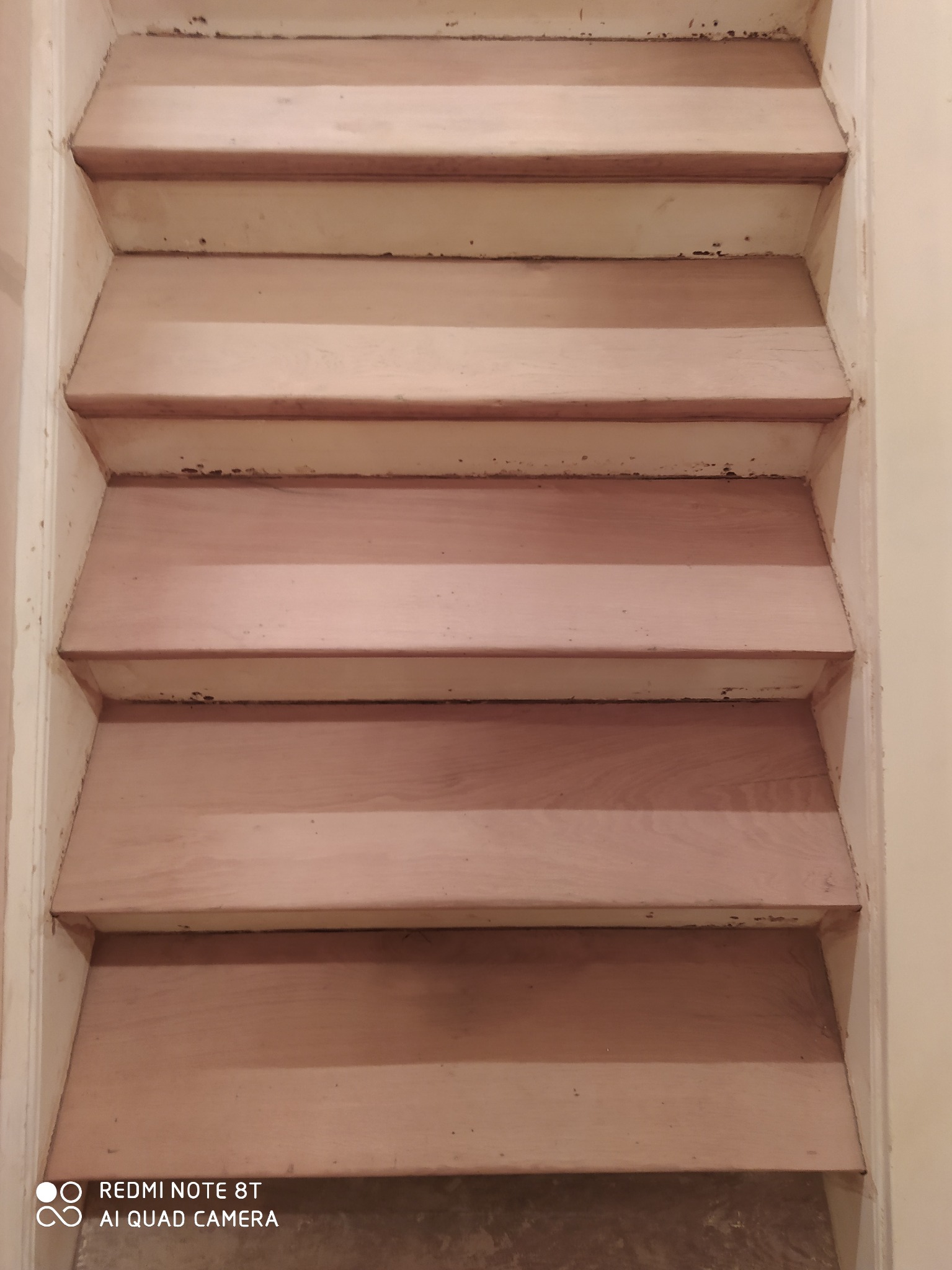 Klatka schodowa z drewnianymi stopniami w trakcie renowacji, widoczne ślady po starej farbie i przygotowanie do dalszych prac wykończeniowych.