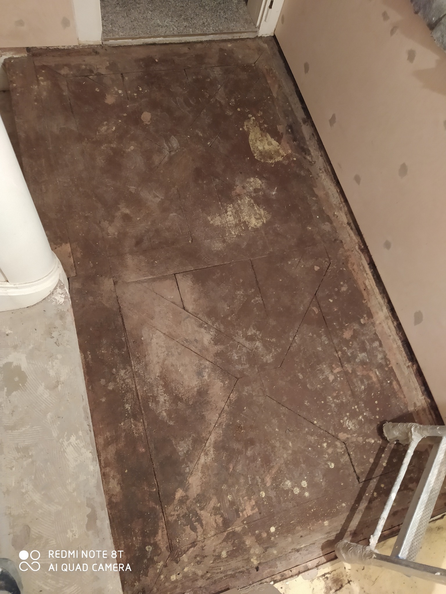 Zdemontowana, stara podłoga drewniana z widocznymi śladami użytkowania, przygotowana do remontu, z częściowo wykończoną ścianą i fragmentem drabiny w rogu.