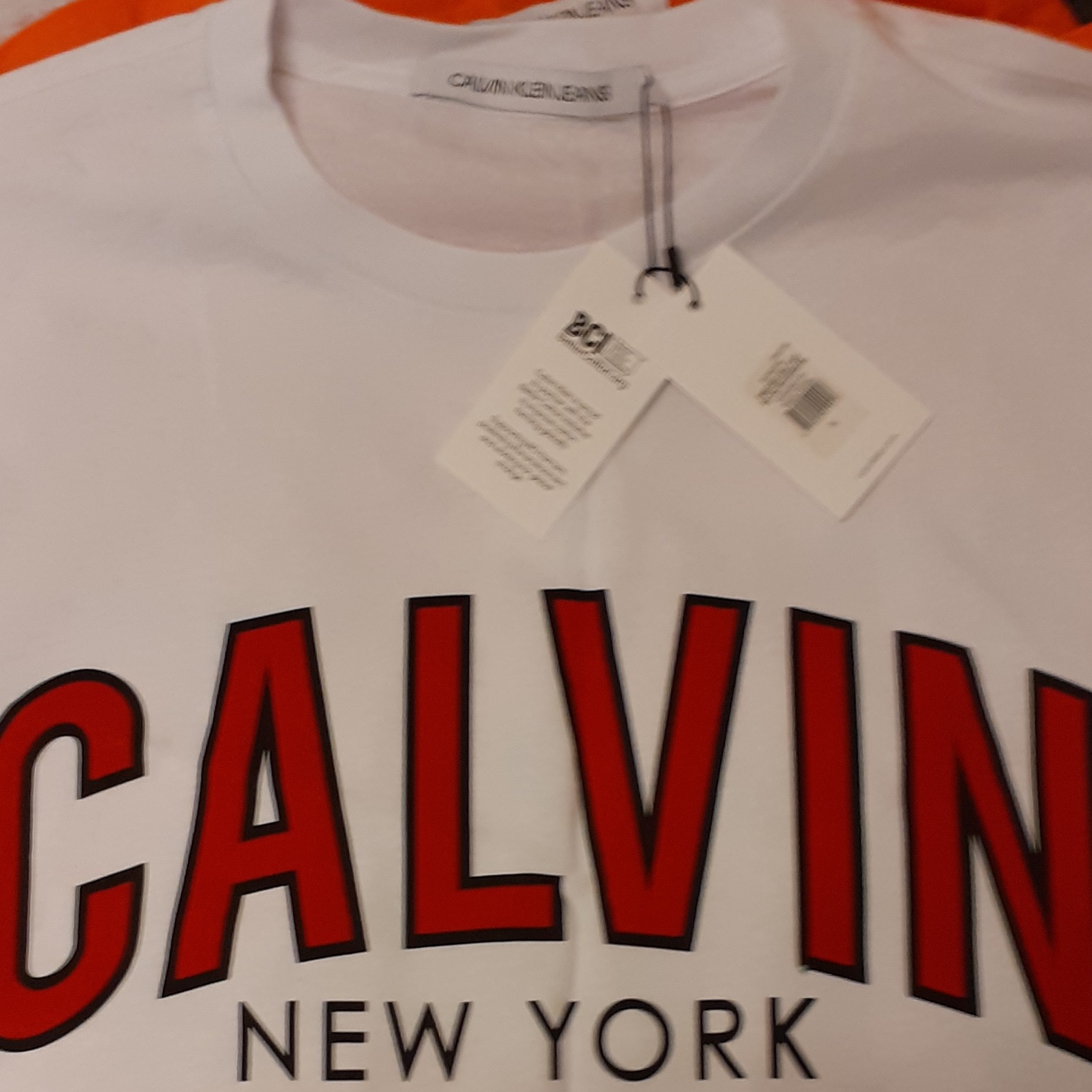 Biała koszulka Calvin Klein Jeans z czerwonym napisem CALVIN NEW YORK i metką BCI.