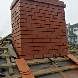 Usługi Dekarskie - Murowany komin z czerwonej cegły na dachu w trakcie budowy, widoczne narzędzia i dachówki.