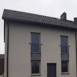 Nowoczesny budynek dwukondygnacyjny z szarymi oknami z balustradami i ciemnymi drzwiami wejściowymi, widok z zewnątrz.