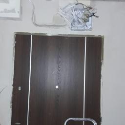 Adrian Maśny - Montaż drzwi wewnętrznych z widoczną puszką elektryczną nad ościeżnicą i fragmentem drabiny.