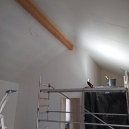 Tp bud - Pokój na poddaszu w trakcie malowania, widoczne rusztowanie, drabina i zabezpieczona folią ściana, sufit pomalowany na biało, widoczna drewniana belka stropowa.