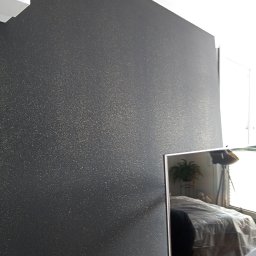 Tp bud - Ściana pomalowana na ciemny kolor z delikatnym, złotym połyskiem widoczna w perspektywie, odbicie sypialni w lustrze obok.