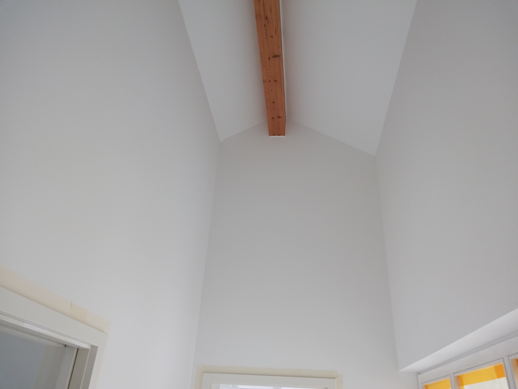 Wysoki, jasny pokój po malowaniu, z drewnianą belką stropową i oknami w dolnej części kadru.