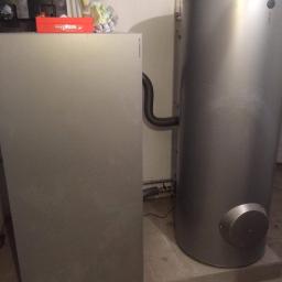 D.M - Szara kotłownia z dwoma zbiornikami, z których jeden jest pionowy i cylindryczny, a drugi płaski i prostokątny, z czerwonym pudełkiem narzędzi Viessmann na górze płaskiego zbiornika.