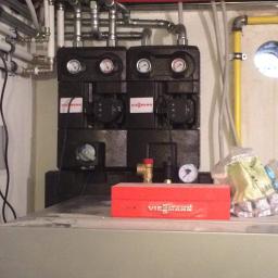 D.M - Dwa czarne moduły Viessmann z manometrami i pompami obiegowymi, widoczne rury instalacji, żółta rura gazowa, czerwona skrzynka narzędziowa Viessmann na szarym urządzeniu.