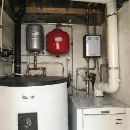Kompletna instalacja centralnego ogrzewania z dwoma zbiornikami wyrównawczymi Watts, piecem Vaillant i rozbudowaną siecią rur w małym pomieszczeniu, widok z bliska.