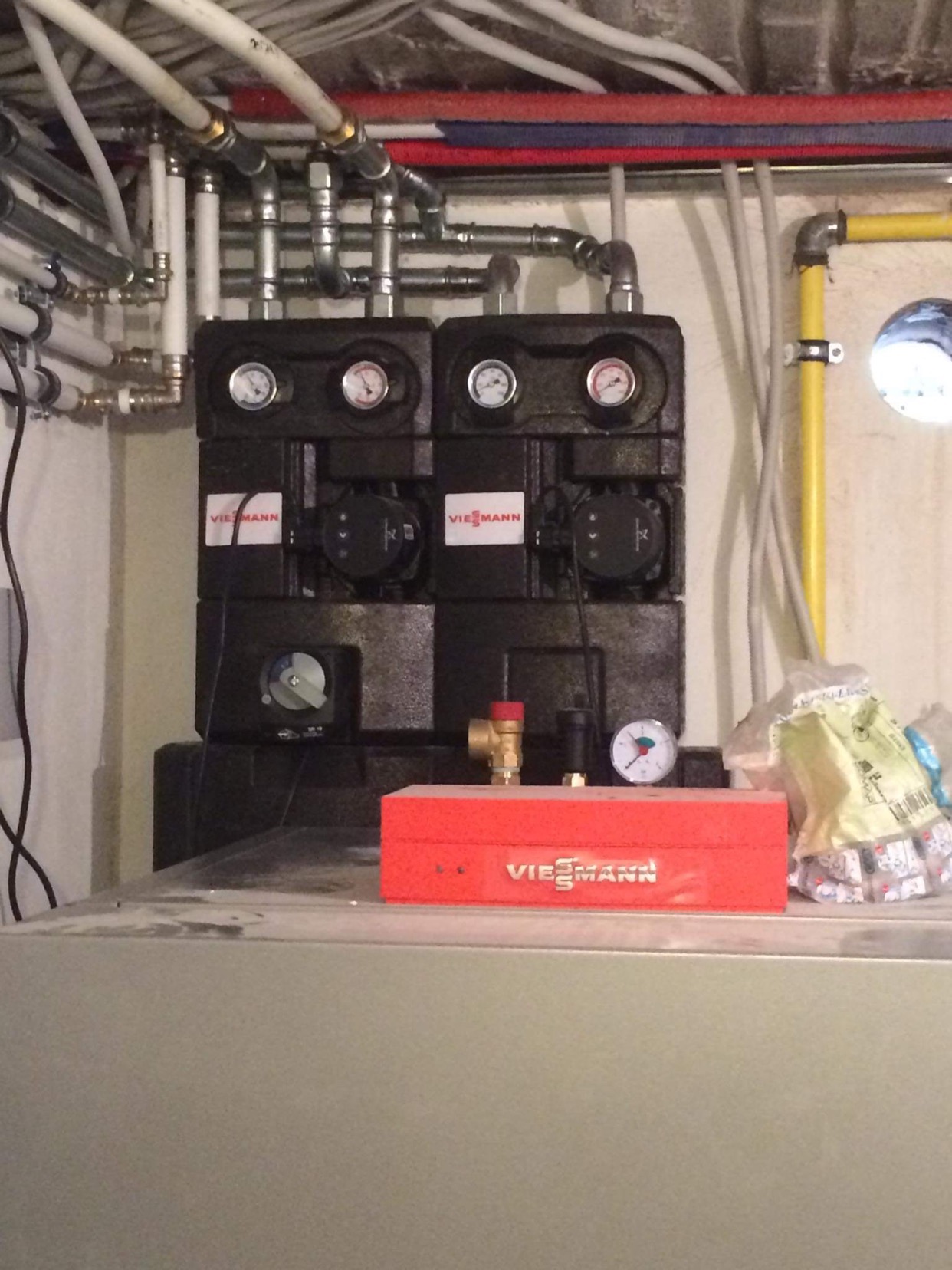 Dwa czarne moduły Viessmann z manometrami i pompami obiegowymi, widoczne rury instalacji, żółta rura gazowa, czerwona skrzynka narzędziowa Viessmann na szarym urządzeniu.