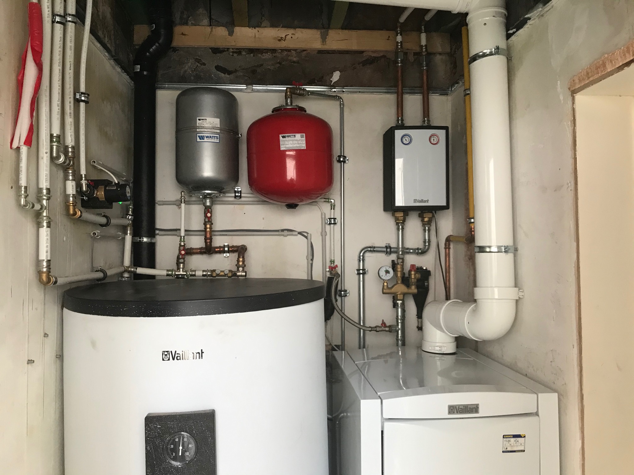 Kompletna instalacja centralnego ogrzewania z dwoma zbiornikami wyrównawczymi Watts, piecem Vaillant i rozbudowaną siecią rur w małym pomieszczeniu, widok z bliska.