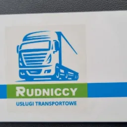 Wizytówka firmy transportowej Rudniccy z niebieskim logo ciężarówki na białym tle, leżąca na czarnej powierzchni.