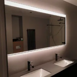 Nowoczesna łazienka w Międzyzdrojach z podświetlanym lustrem nad podwójną umywalką z czarnymi bateriami, widoczna kabina prysznicowa w tle.